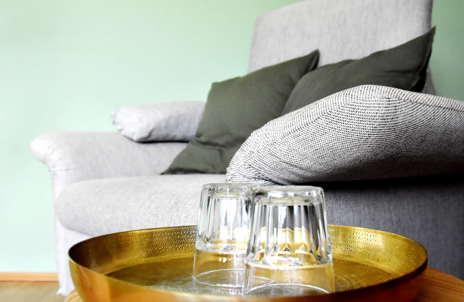 Graues Sofa mit Kissen; davor stehen zwei Wassergläser auf einem goldfarbenen Tablett.
