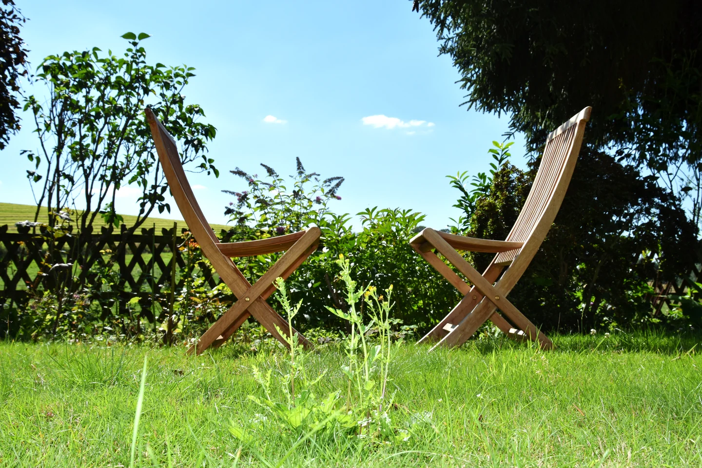 Zwei einander zugewandte Holzstühle im grünen Gartenbereich der Praxis unter blauem Himmel.